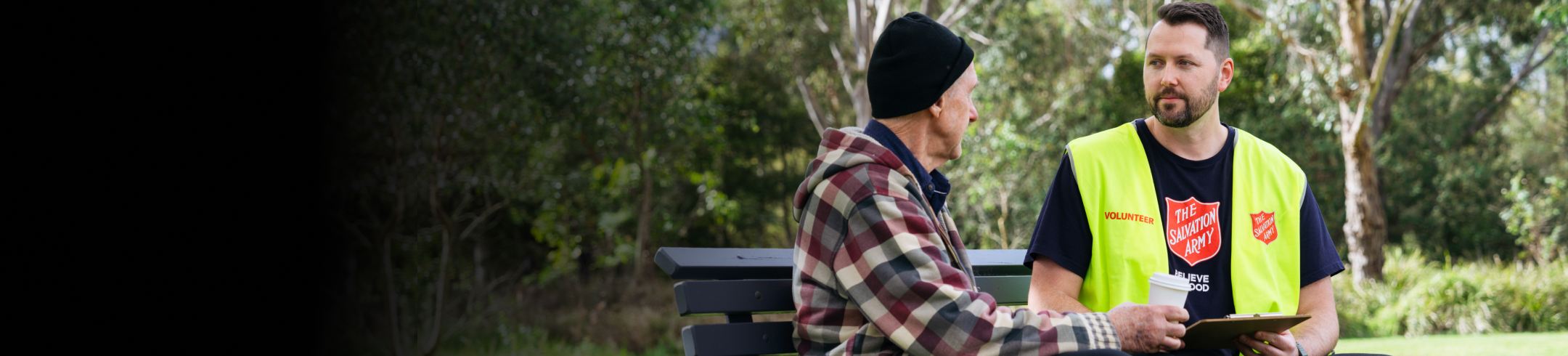 A Salvos volunteer and an older gentleman share a park bench, a coffee and chat.